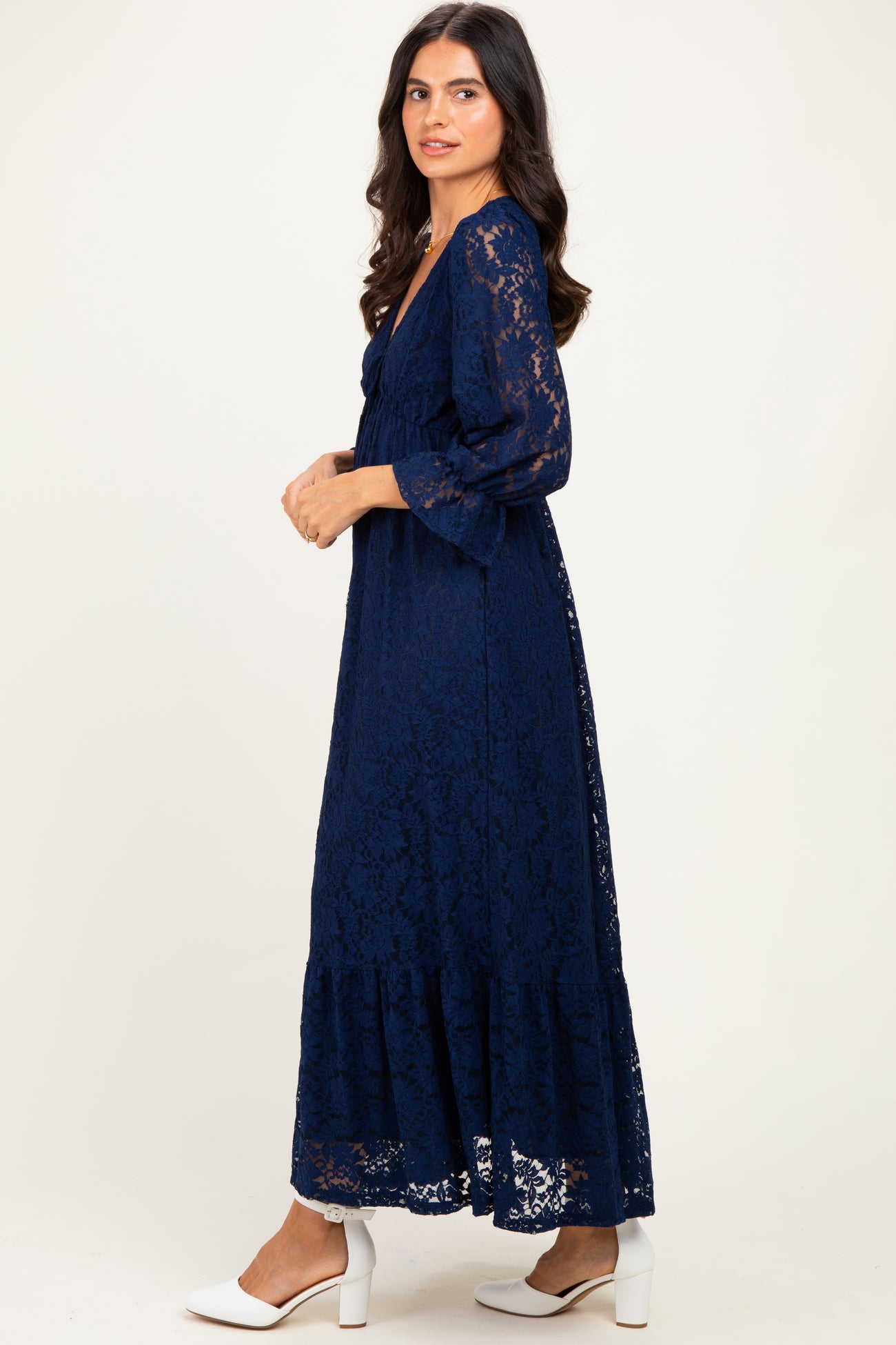woman wearing a navy blue lace maxi dress with long sleeves and a tiered skirt, standing in profile