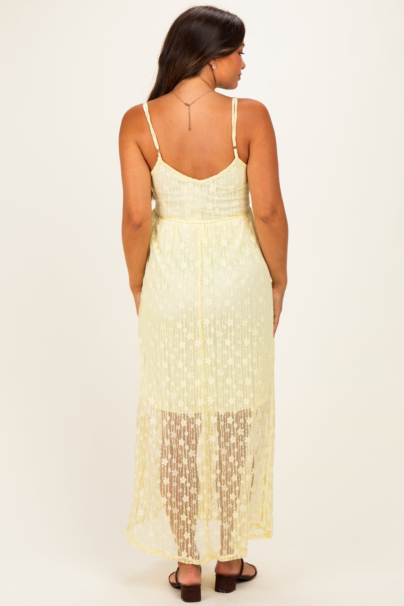 woman wearing a yellow lace maternity dress with a high-low hem and spaghetti straps, view from the back