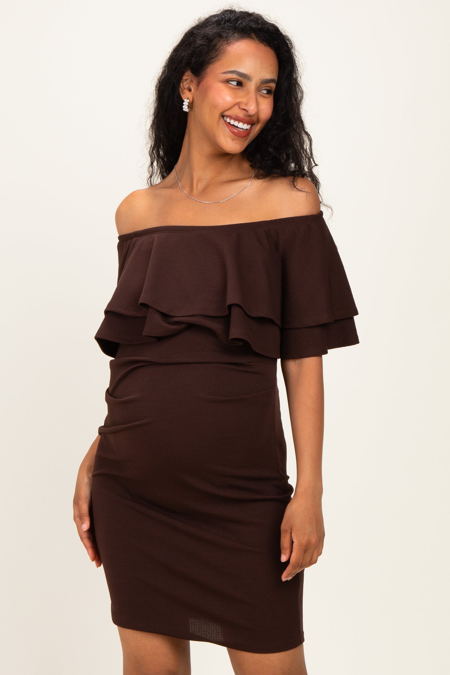 woman wearing a brown off-the-shoulder maternity dress with ruffle details and a visible baby bump