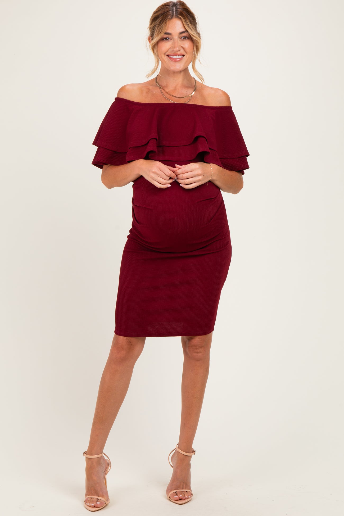 woman wearing a burgundy off-the-shoulder maternity dress with ruffle details and a visible baby bump