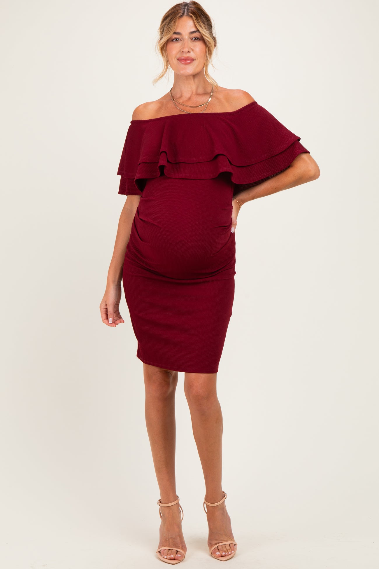 woman wearing a burgundy off-the-shoulder maternity dress with ruffle details and a visible baby bump