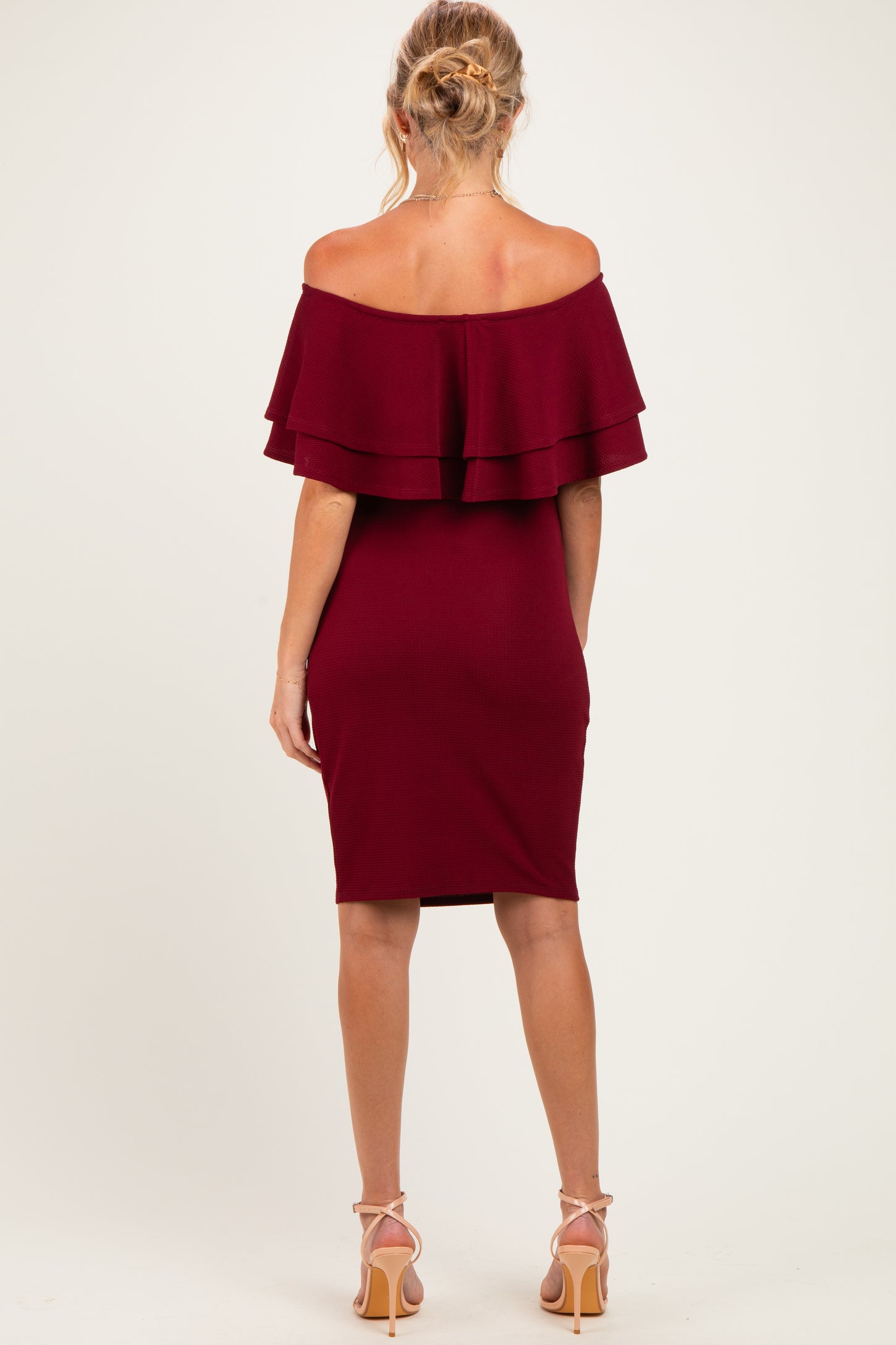 woman wearing a burgundy off-the-shoulder maternity dress with layered ruffles and a fitted silhouette