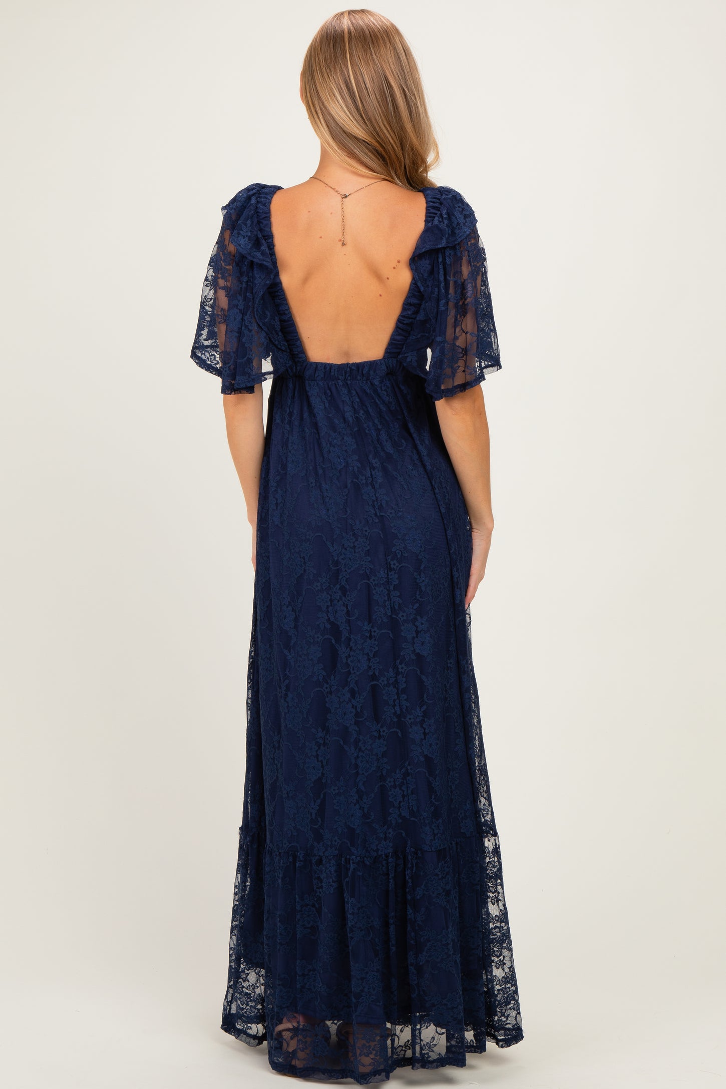 woman wearing a navy blue lace maxi dress with a deep back and short flutter sleeves