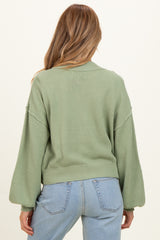 woman wearing a light green maternity sweater with balloon sleeves, shown from the back