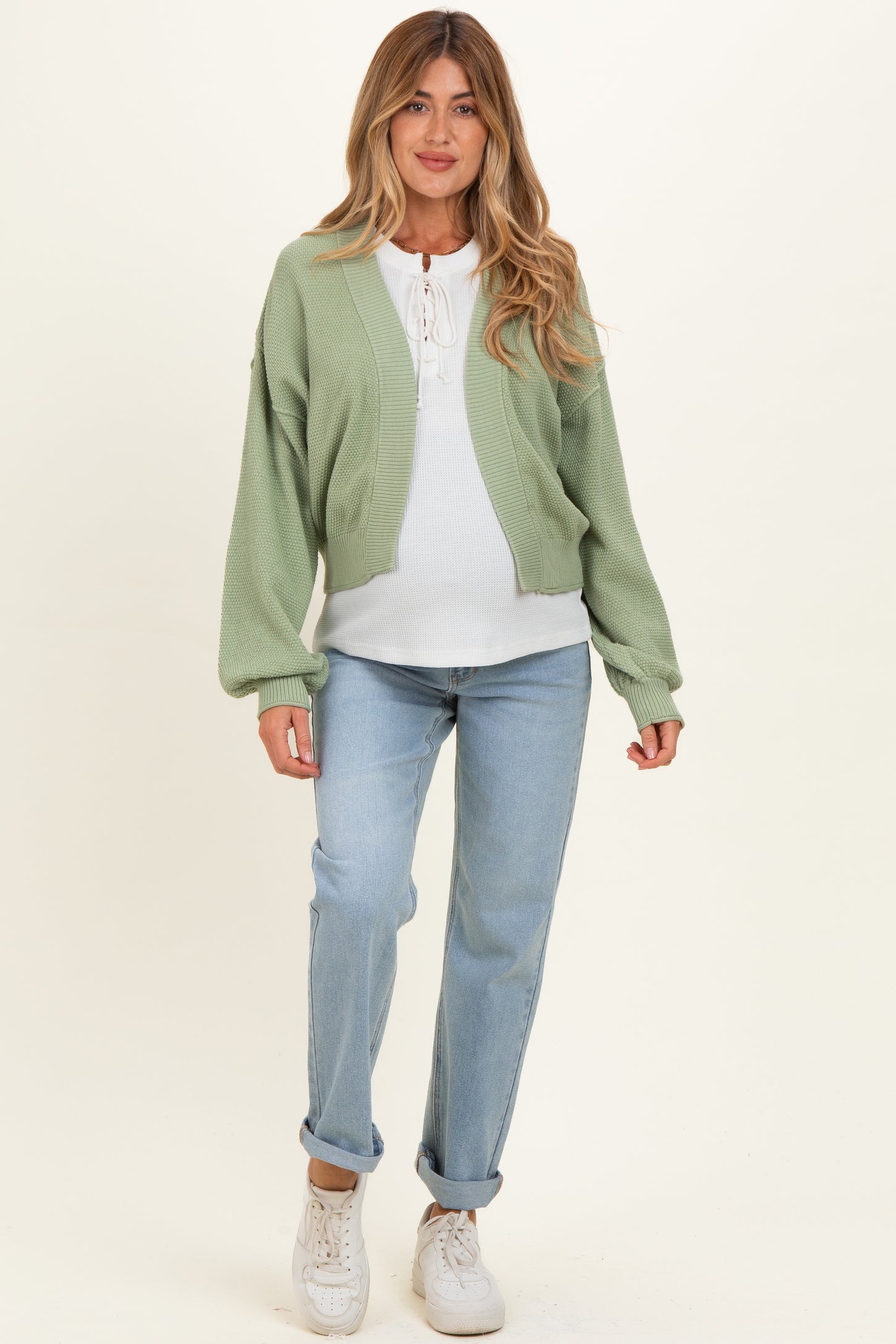 woman wearing a green knitted maternity cardigan over a white top and blue maternity jeans with a visible baby bump