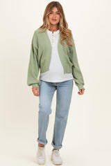 woman wearing a green knitted maternity cardigan over a white top and blue maternity jeans with a visible baby bump