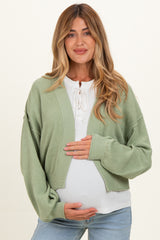 woman wearing a green cropped maternity cardigan over a white top and holding her baby bump