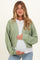woman wearing a green cropped maternity cardigan over a white top and holding her baby bump