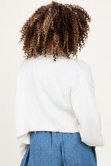 woman wearing a white cropped maternity sweater, viewed from the back, styled with blue polka dot maternity pants