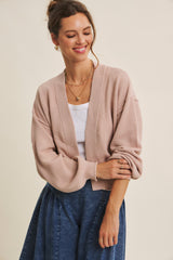 woman wearing a light pink oversized cardigan over a white top and a denim skirt, smiling and standing with one hand on her hip