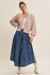 woman wearing a light pink oversized cardigan and a flowy denim skirt with pleats