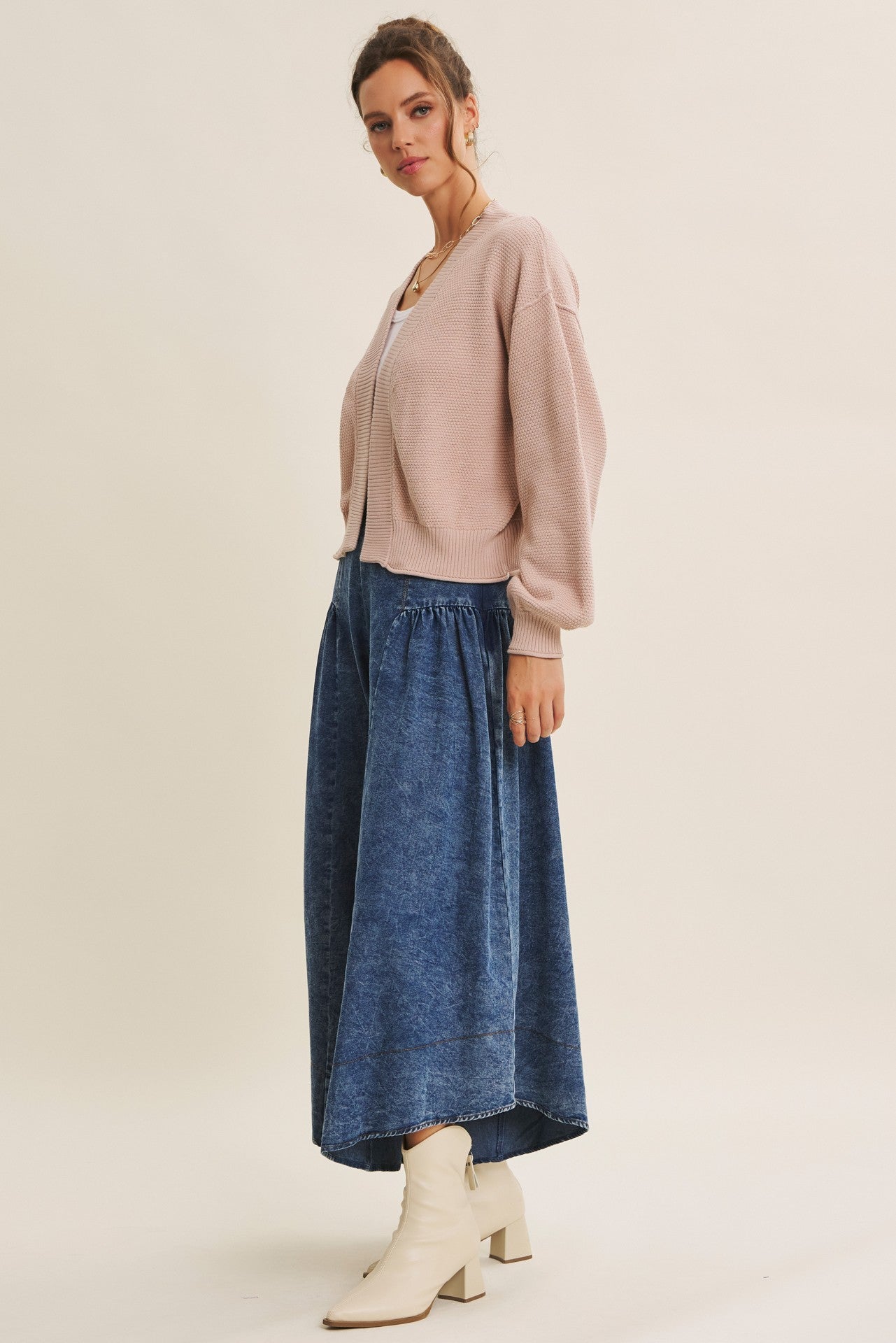 woman wearing a light pink oversized cardigan and a denim maxi skirt, styled with white ankle boots