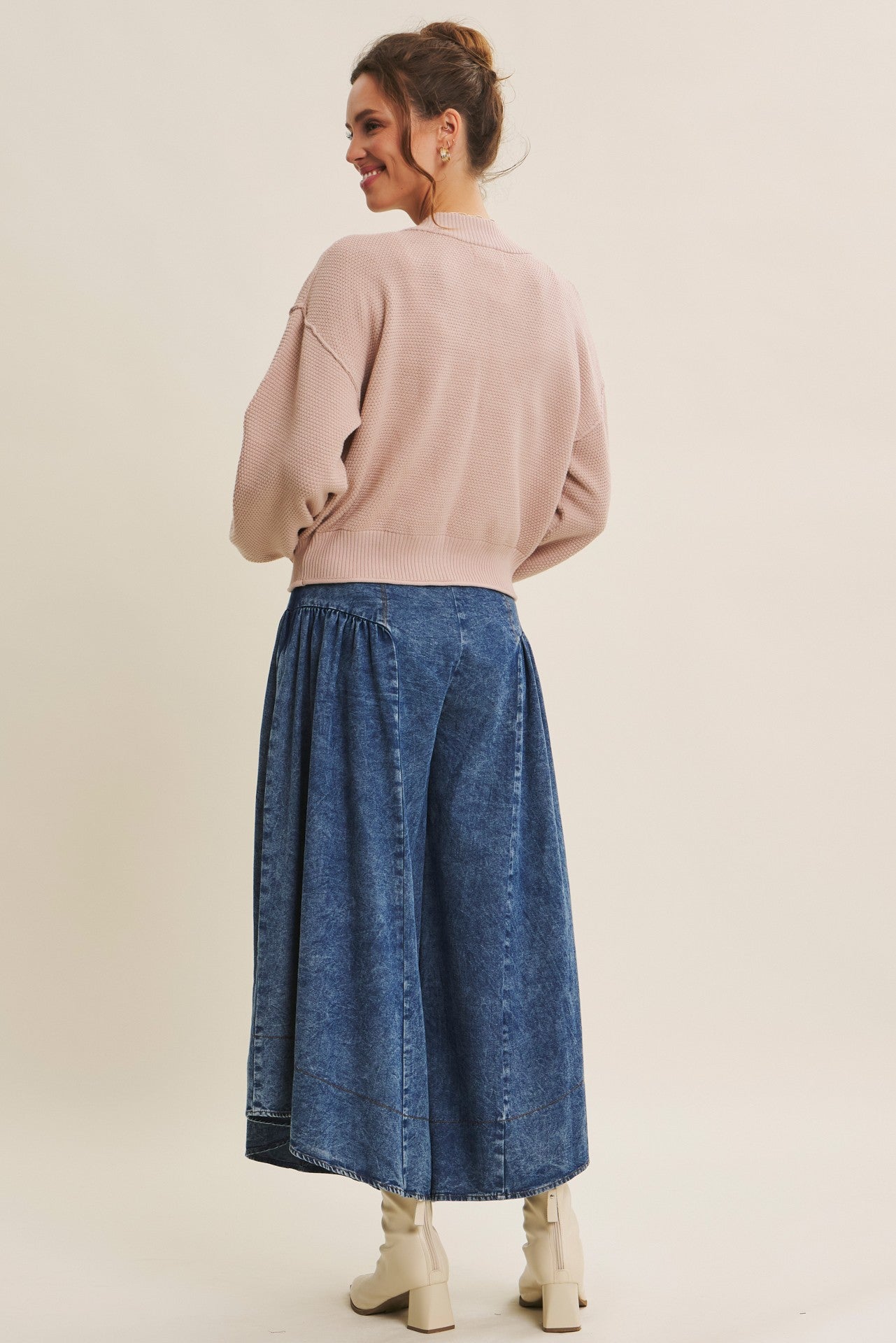 woman wearing a light pink cropped sweater and a long denim skirt, viewed from the back
