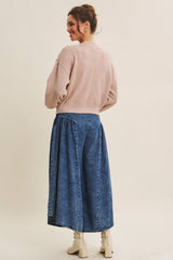 woman wearing a light pink cropped sweater and a long denim skirt, viewed from the back