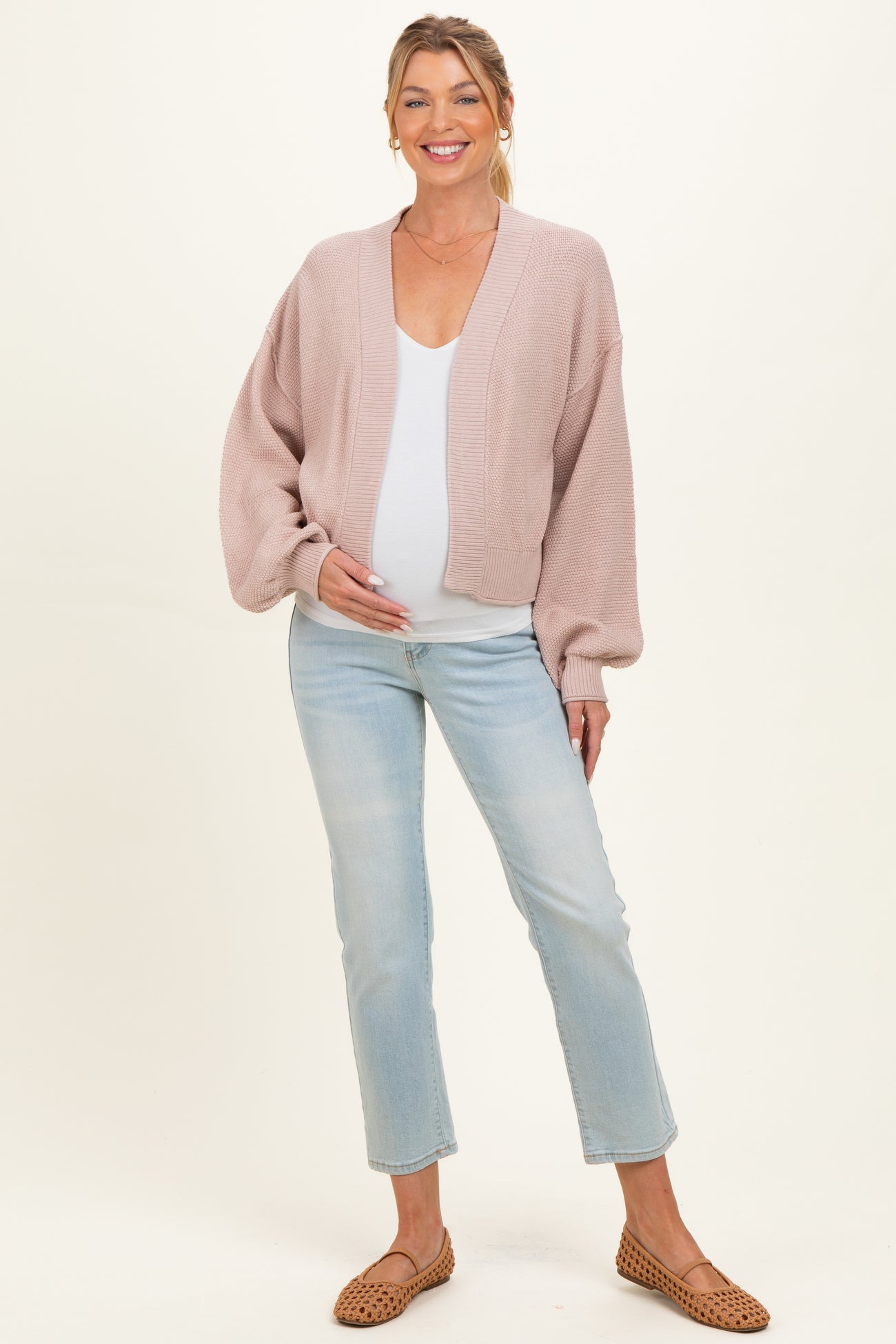 woman wearing a light pink maternity cardigan over a white top and showing her baby bump, paired with light wash jeans