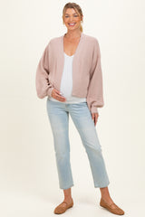 woman wearing a light pink maternity cardigan over a white top and showing her baby bump, paired with light wash jeans