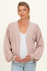 woman wearing a light pink maternity cardigan over a white top and holding her baby bump