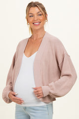 woman wearing a light pink maternity cardigan over a white tank top and holding her baby bump