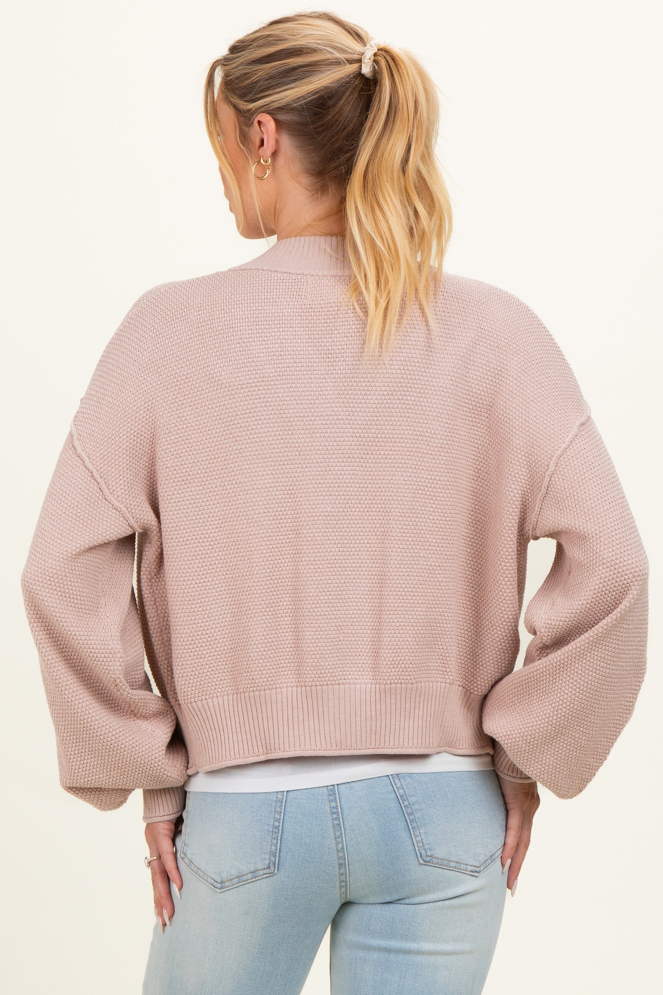 woman wearing a light pink cropped maternity cardigan with balloon sleeves, viewed from the back