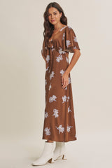 woman wearing a brown floral maxi dress with short sleeves and a tie detail at the waist, paired with white ankle boots