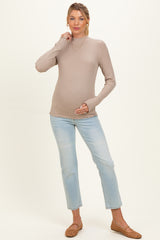 woman wearing a light beige maternity long sleeve top and blue jeans, gently holding her baby bump