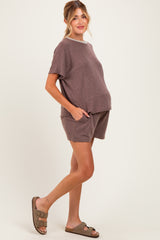 woman wearing a brown short sleeve maternity top and matching shorts, gently cradling her baby bump