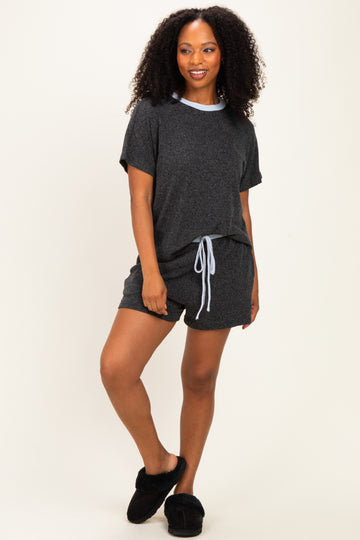 woman wearing a dark gray short sleeve loungewear set with a light blue trim and drawstring shorts, paired with black slippers