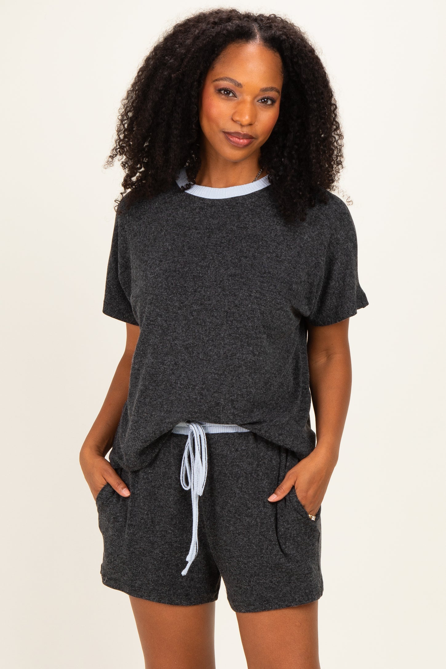 woman wearing a grey short sleeve loungewear set with a blue trim and pockets in the shorts