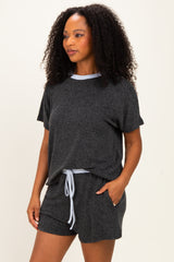woman wearing a dark gray short sleeve lounge set with a light blue trim and drawstring shorts, posing with one hand in pocket