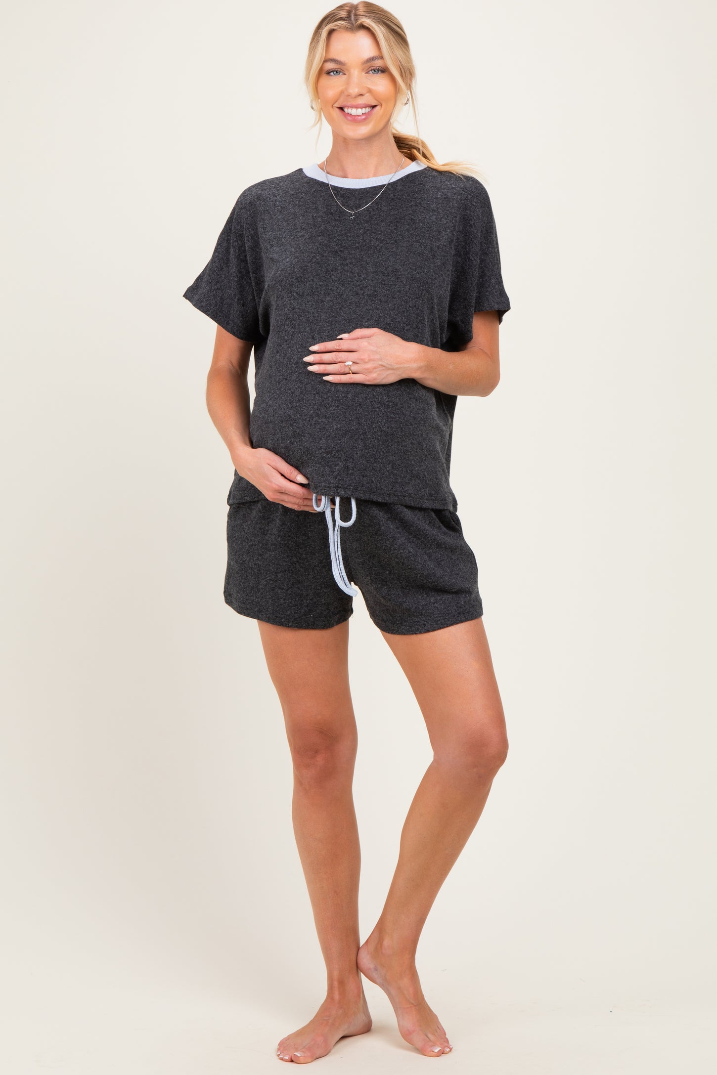 woman wearing a black maternity loungewear set with a loose t-shirt and shorts, cradling her baby bump