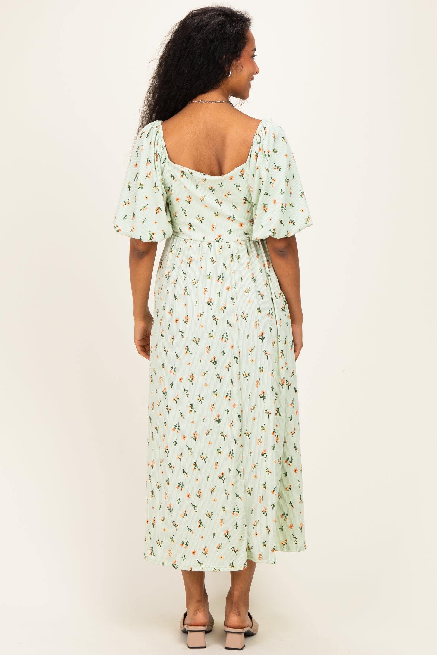 woman wearing a mint green floral print maternity dress with short puff sleeves and a flowy midi length