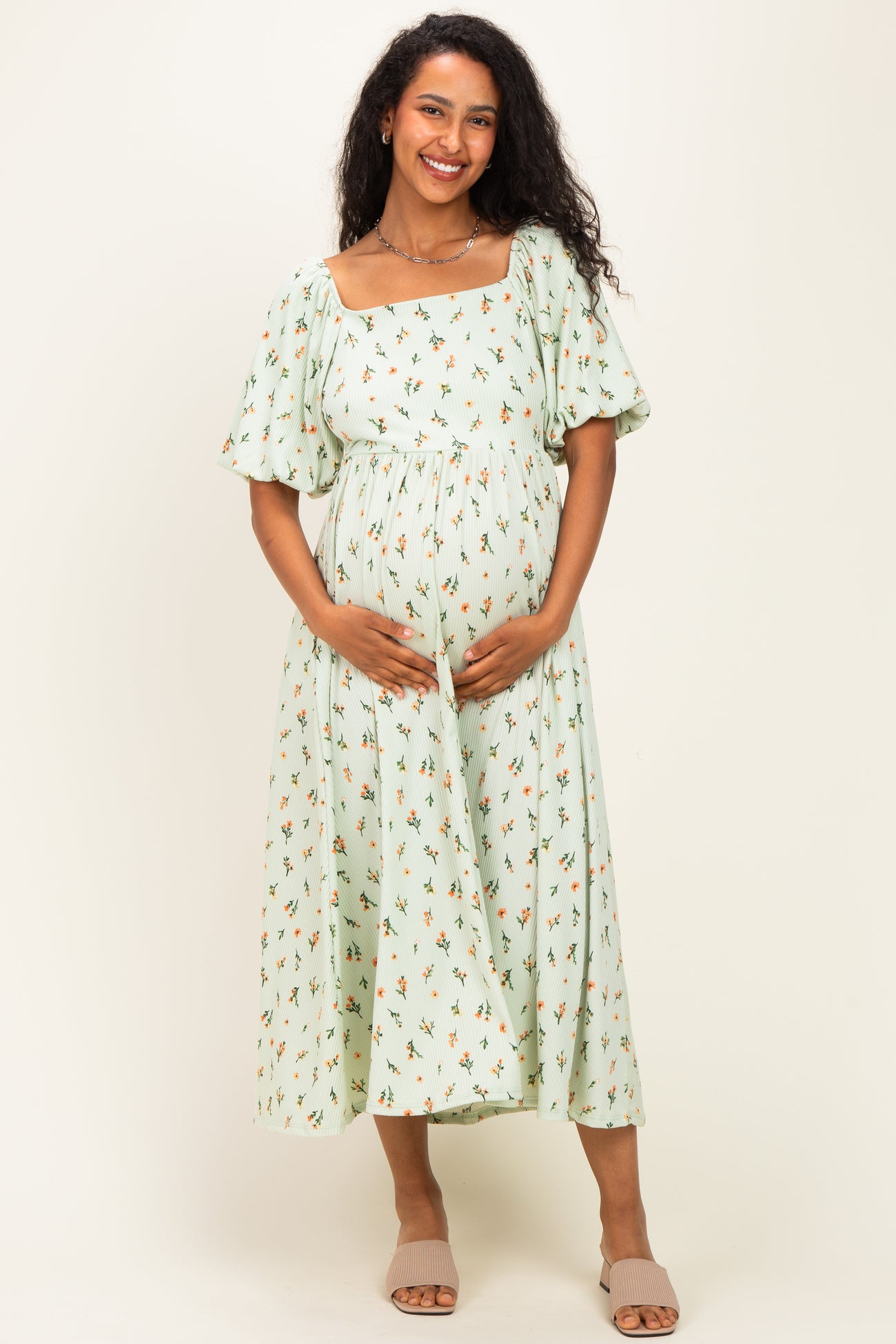 woman wearing a mint green floral print maternity dress with short puff sleeves and holding her baby bump