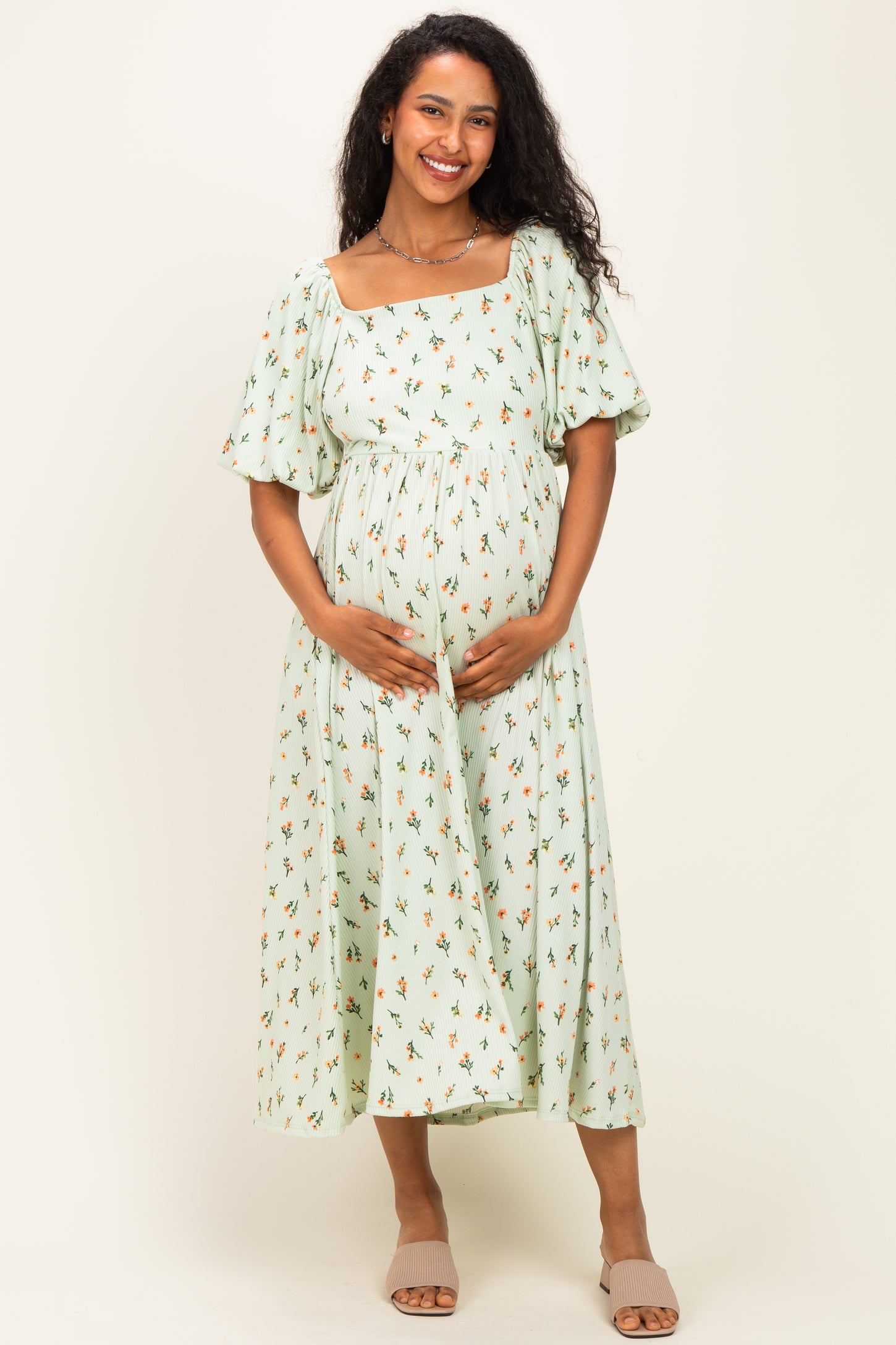 woman wearing a mint green floral print maternity dress with short puff sleeves and holding her baby bump