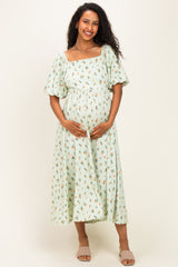 woman wearing a mint green floral print maternity dress with short puff sleeves and holding her baby bump