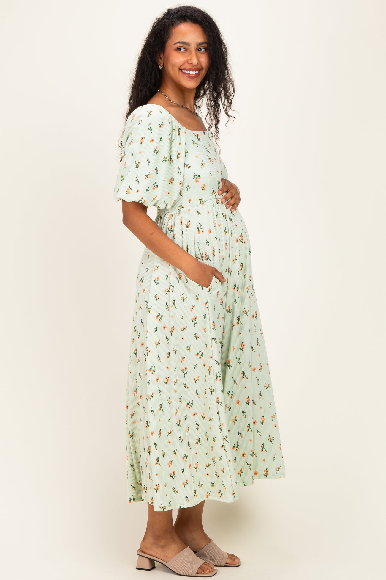 woman wearing a mint green floral maternity dress with puff sleeves and pockets, gently cradling her baby bump