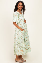 woman wearing a mint green floral maternity dress with puff sleeves and pockets, gently cradling her baby bump