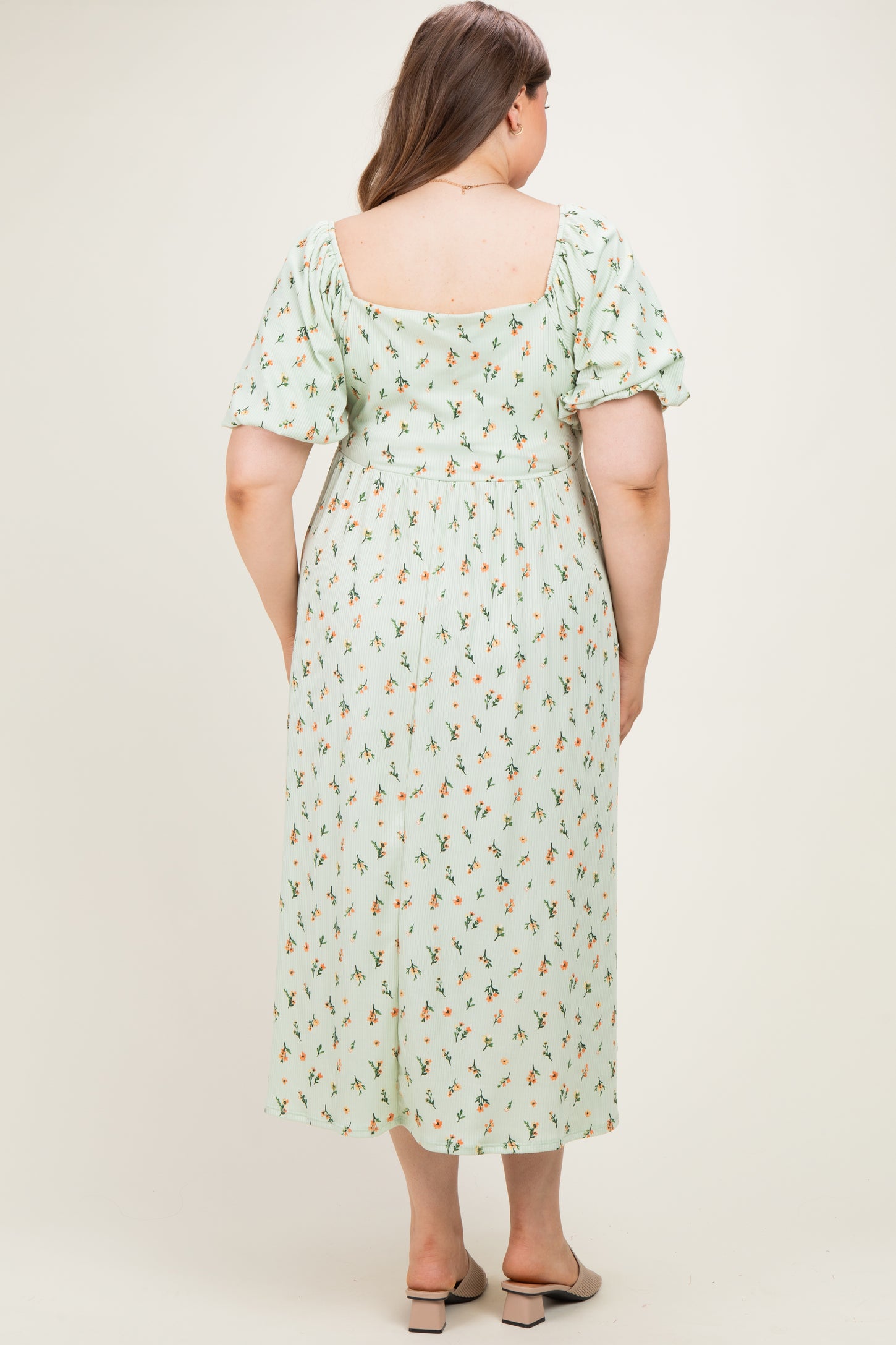 woman wearing a light green floral maternity plus dress with short puff sleeves and a square back design
