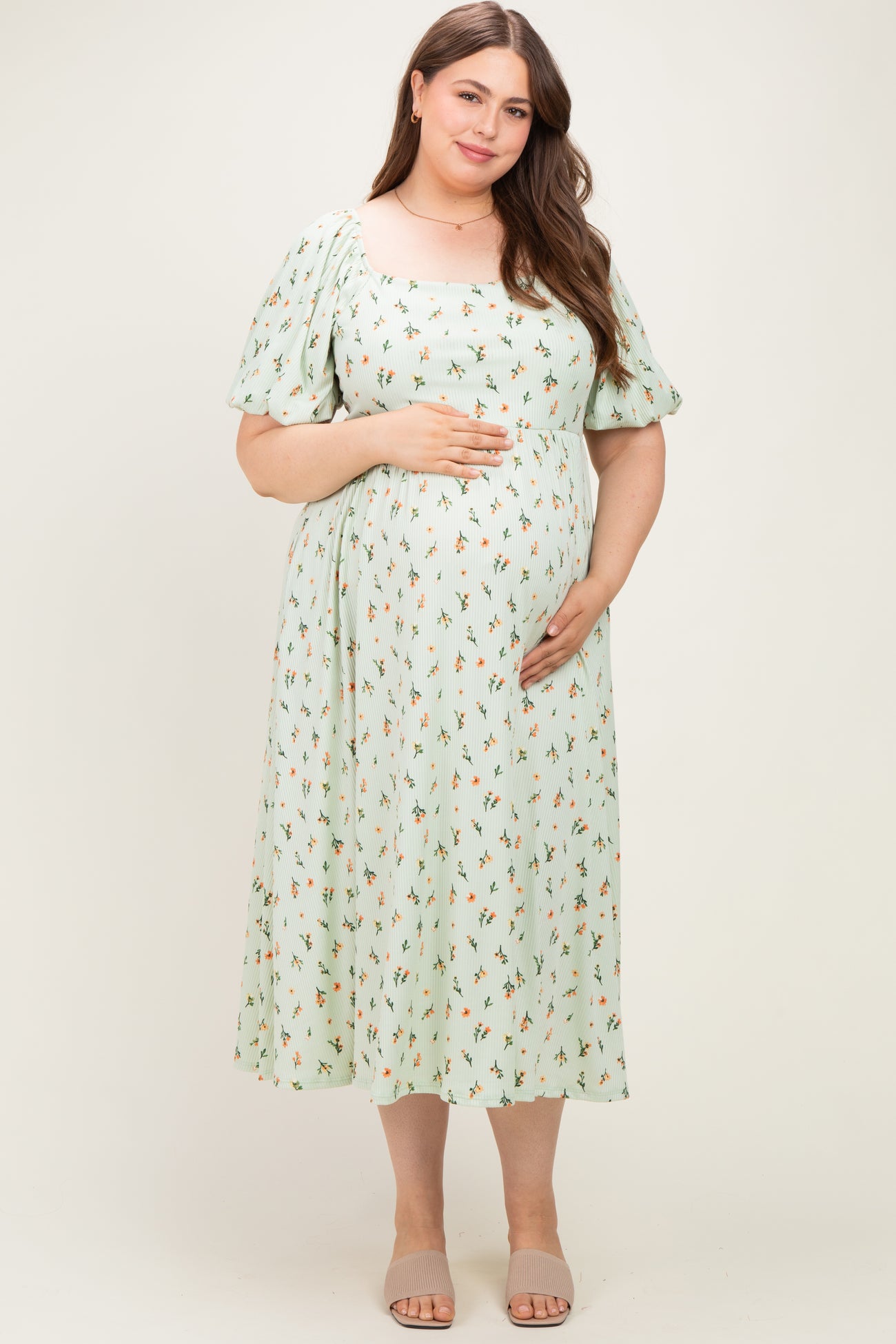 woman wearing a mint green floral maternity dress with puff sleeves and a square neckline, holding her baby bump