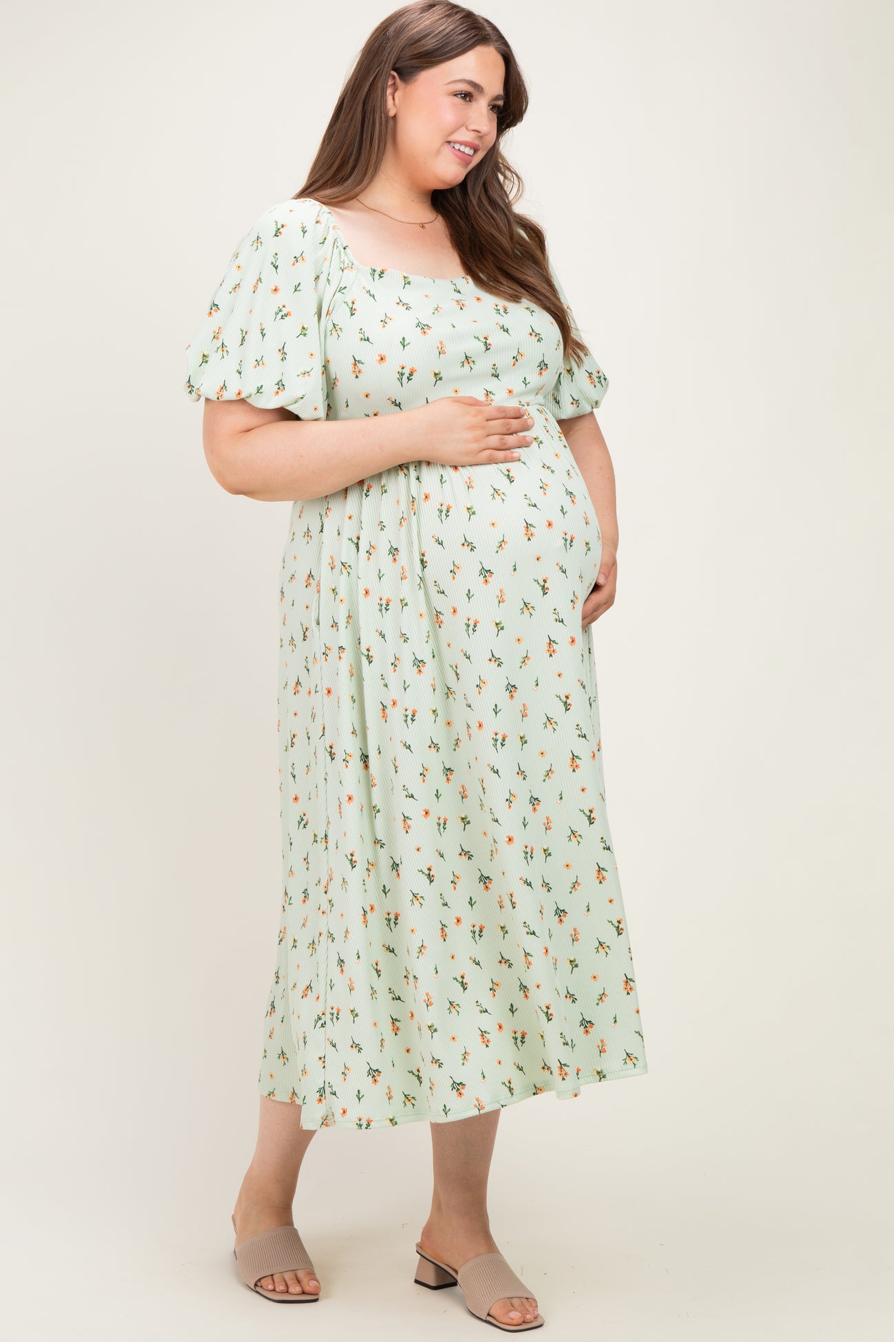 woman wearing a light green floral print maternity dress with puff sleeves and holding her baby bump