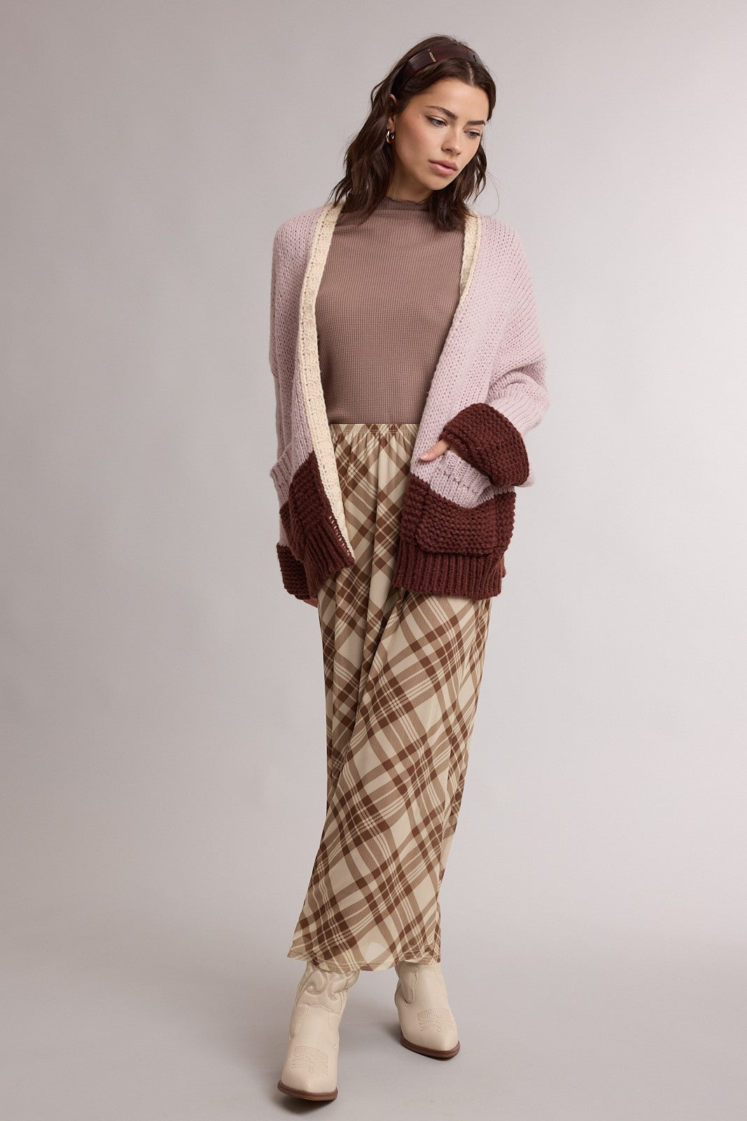 woman wearing a beige ribbed turtleneck, oversized pink and brown cardigan, and plaid wide-leg pants with cream ankle boots