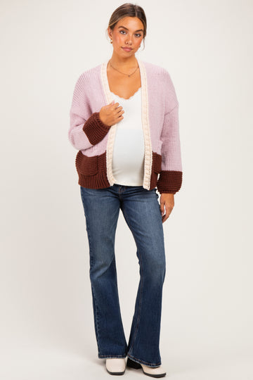 woman wearing a pastel pink and brown maternity cardigan over a white top, paired with flared jeans and showing her baby bump
