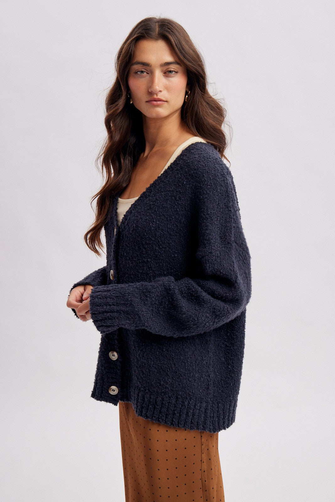 woman wearing a navy blue textured cardigan with buttons over a cream top and a tan polka dot skirt
