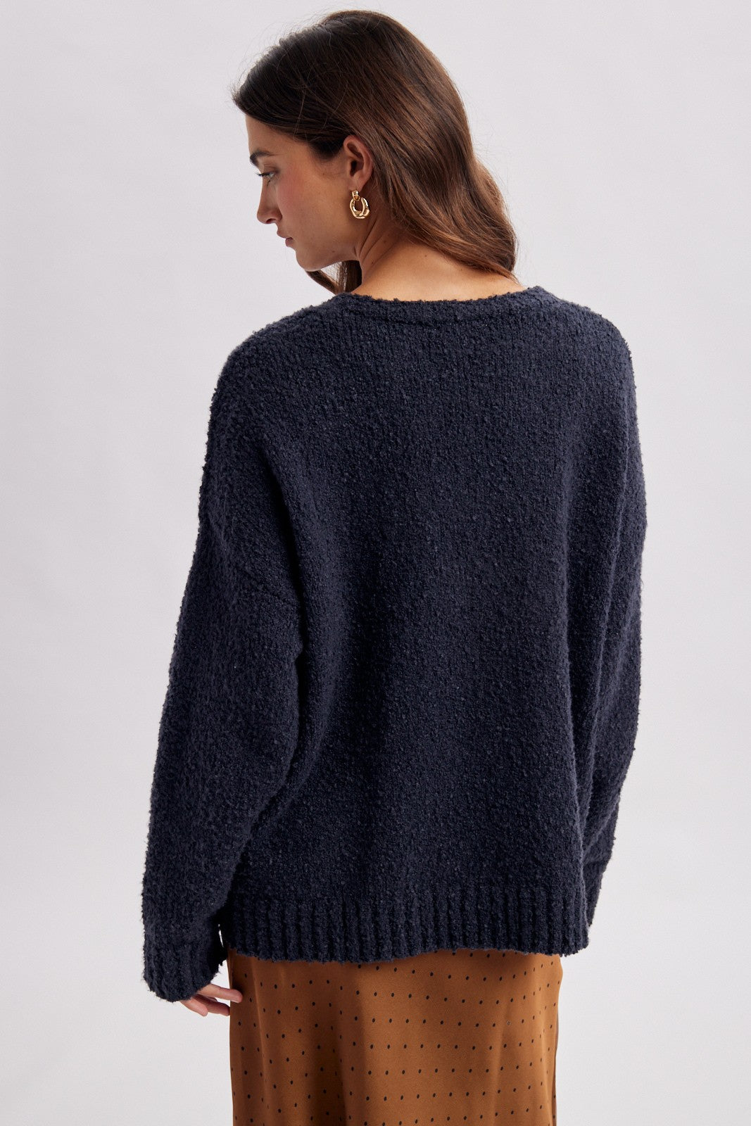 woman wearing a navy blue textured oversized sweater, viewed from the back, paired with a brown polka dot skirt