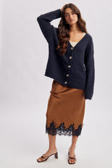 woman wearing a navy oversized cardigan over a cream top and a brown skirt with black lace detailing