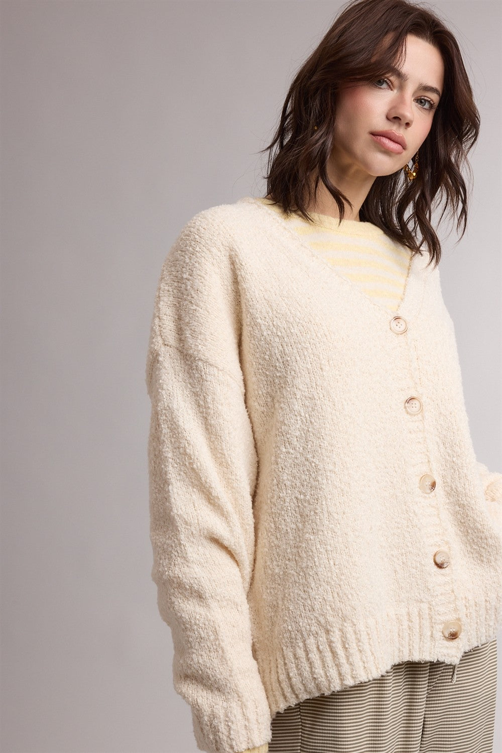 woman wearing a cream textured oversized cardigan with buttons and layered over a striped shirt