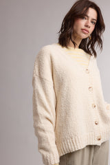 woman wearing a cream textured oversized cardigan with buttons and layered over a striped shirt