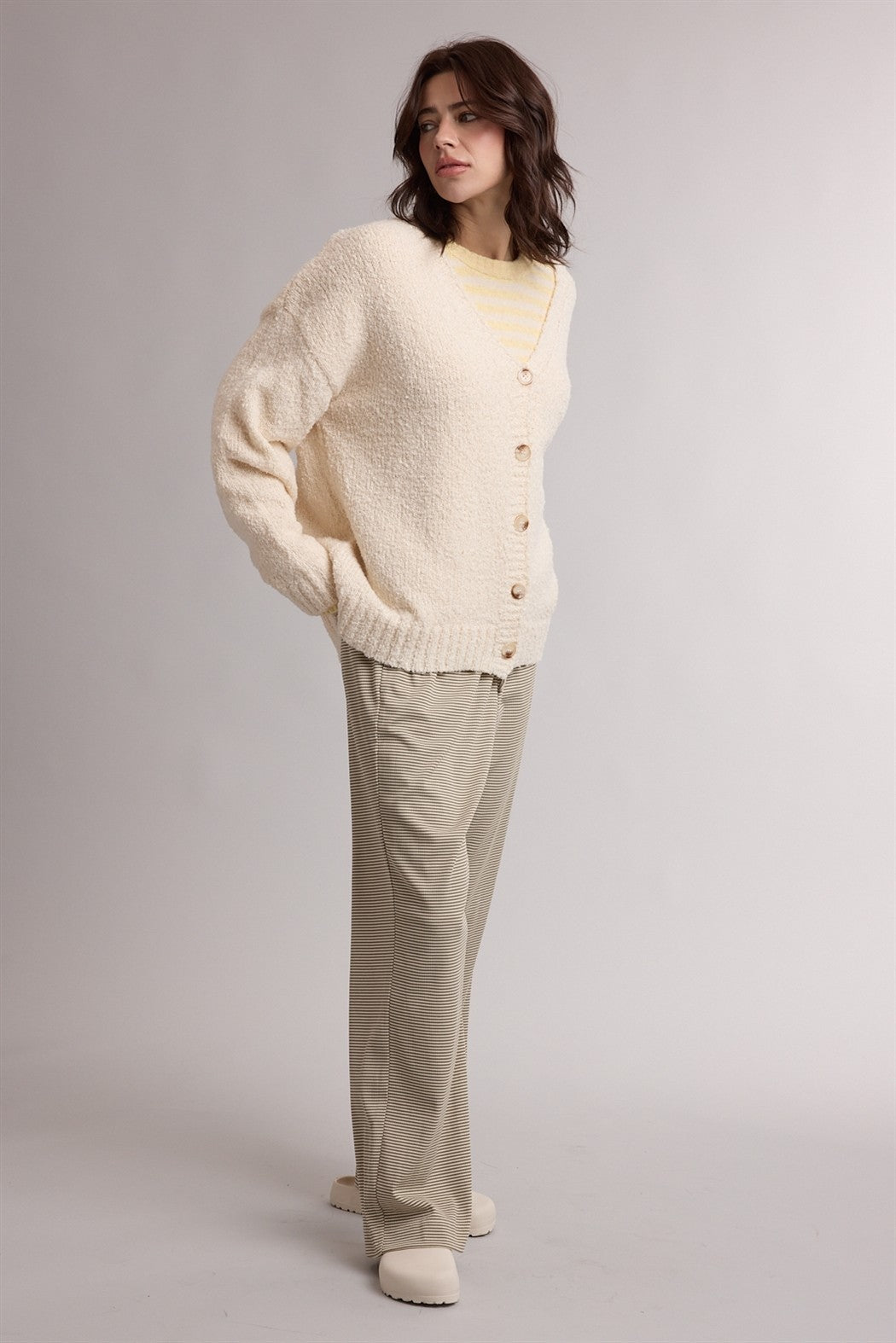 woman wearing a cream oversized cardigan with button closure and paired with light beige wide-leg trousers