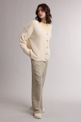 woman wearing a cream oversized cardigan with button closure and paired with light beige wide-leg trousers