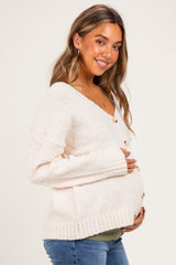 woman wearing a cream knit maternity cardigan and holding her baby bump