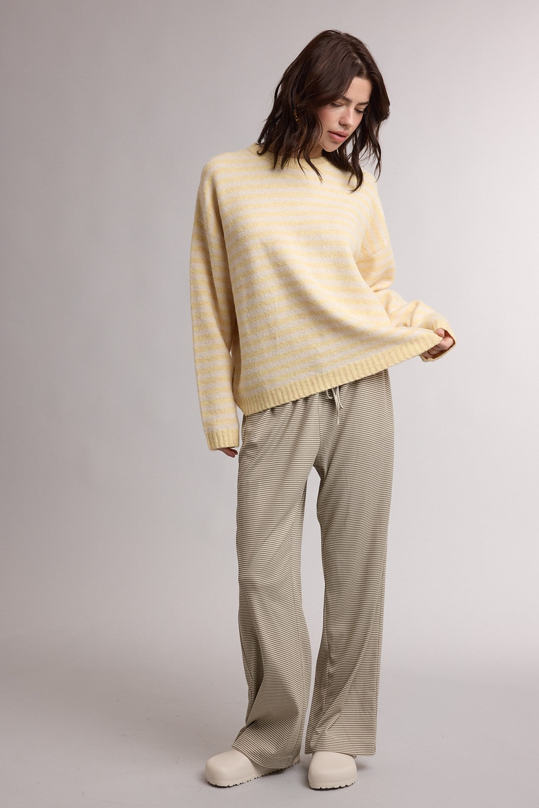 woman wearing a light yellow striped oversized sweater and beige wide-leg pants, standing in a relaxed pose